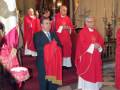 Celebración religiosa en una iglesia con sacerdotes en trajes rojos y un hombre en traje negro en el centro.