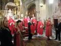 Celebración religiosa en una iglesia con sacerdotes vestidos de rojo y fieles en el altar.
