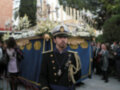 Un hombre vestido con uniforme militar, posiblemente de la Guardia Real, está en un desfile. Detalle de una procesión religiosa o militar con faroles y decoraciones en el fondo, rodeado por espectadores.