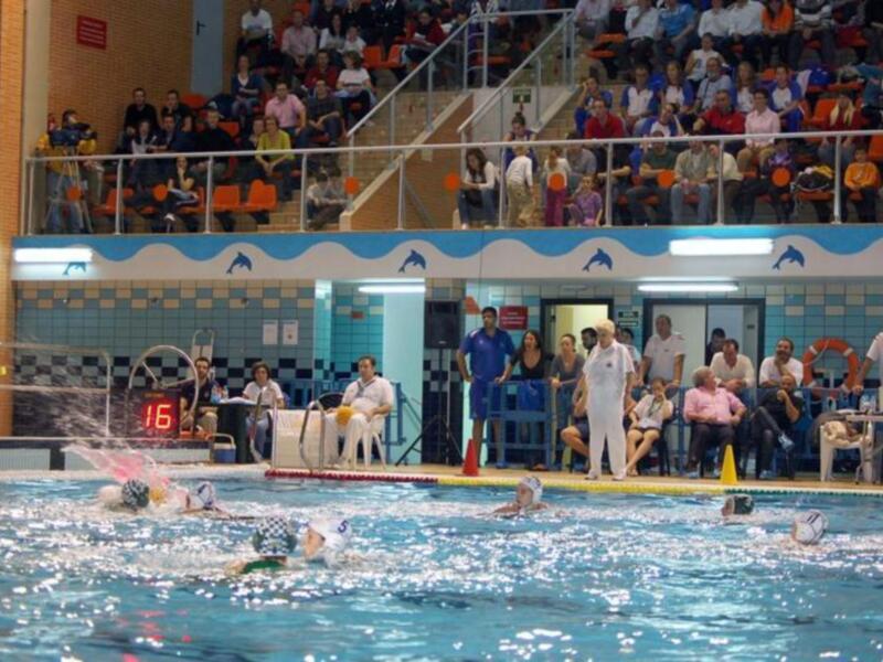 Jugadores de waterpolo en acción durante un partido, con público en las gradas.