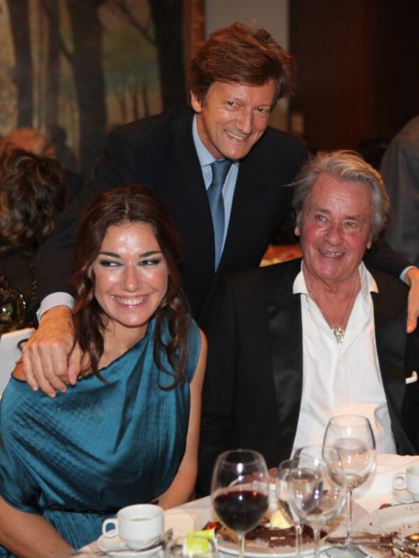 Dos personas sonrientes disfrutan de una cena en un ambiente elegante, rodeadas de vajilla y platos de comida.