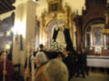 Una procesión religiosa en una iglesia, con una imagen de la Virgen en un catafalco y fieles observando.
