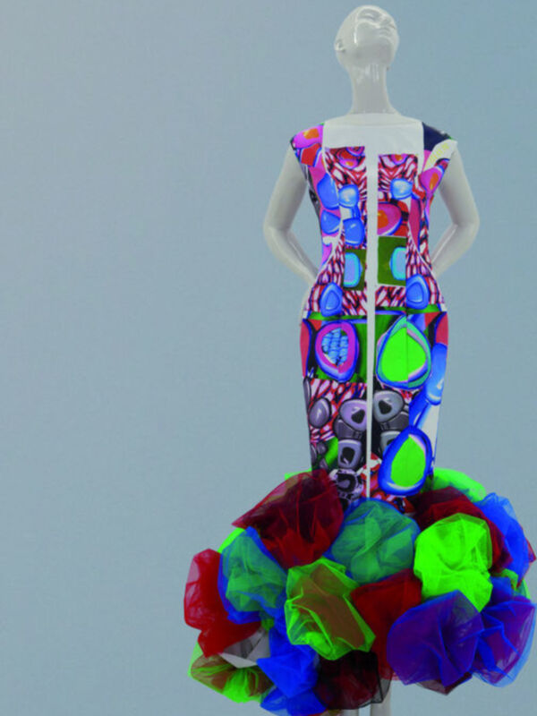 Una figura de maniquí con un vestido de manga corta y falda larga, adornado con patrones geométricos en colores vibrantes como azul, verde, rojo y púrpura. La falda inferior está compuesta por una colección de flores en diferentes colores y texturas. El fondo es un color claro que contrasta con el vestido, enfocando la atención en los detalles del diseño.