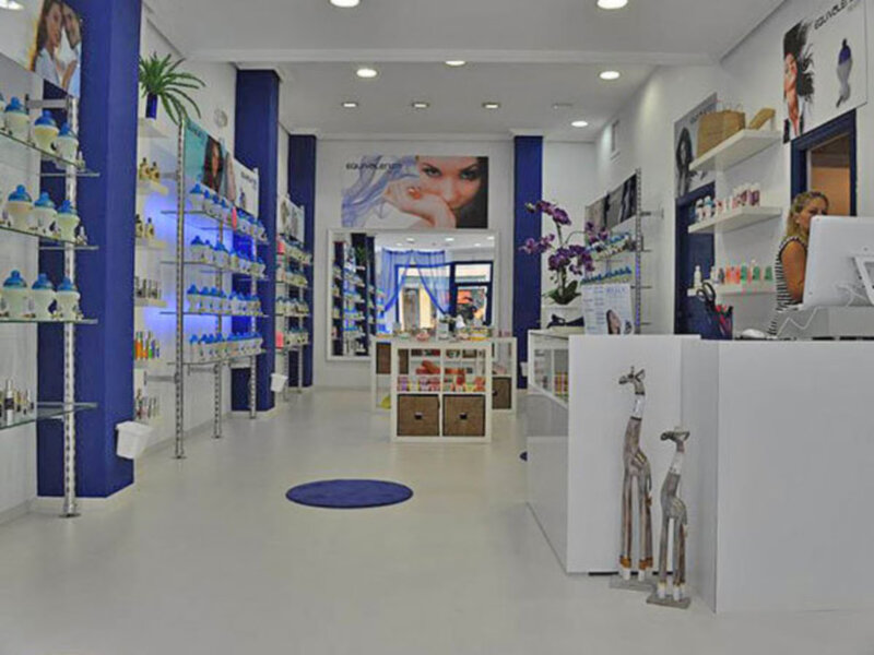 Interior of a modern beauty salon with shelves of products, a counter, and a woman working behind it.
