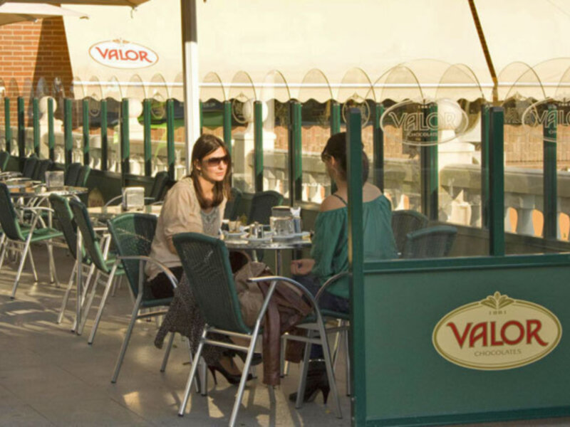 Damas relajándose en una terraza de café con sombrillas de Valor Chocolates.