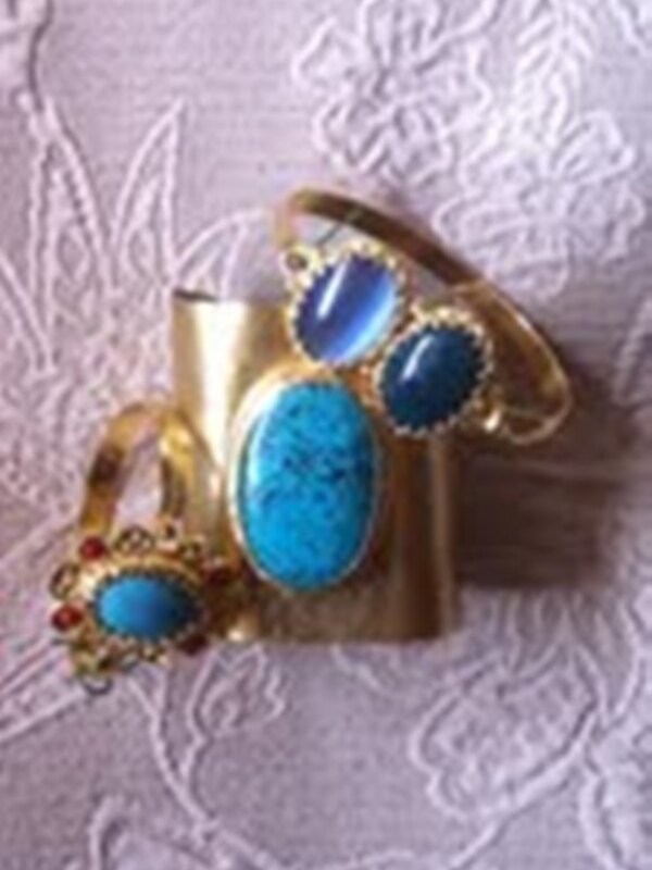 An elegant gold ring adorned with three oval turquoise stones, set against a delicate lace background.