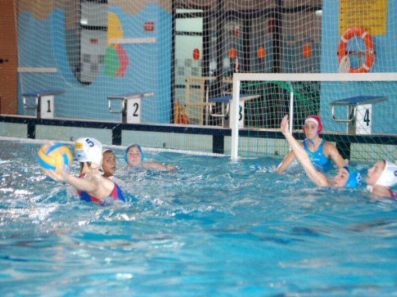Jugadoras de waterpolo en acción durante un partido en una piscina cubierta.