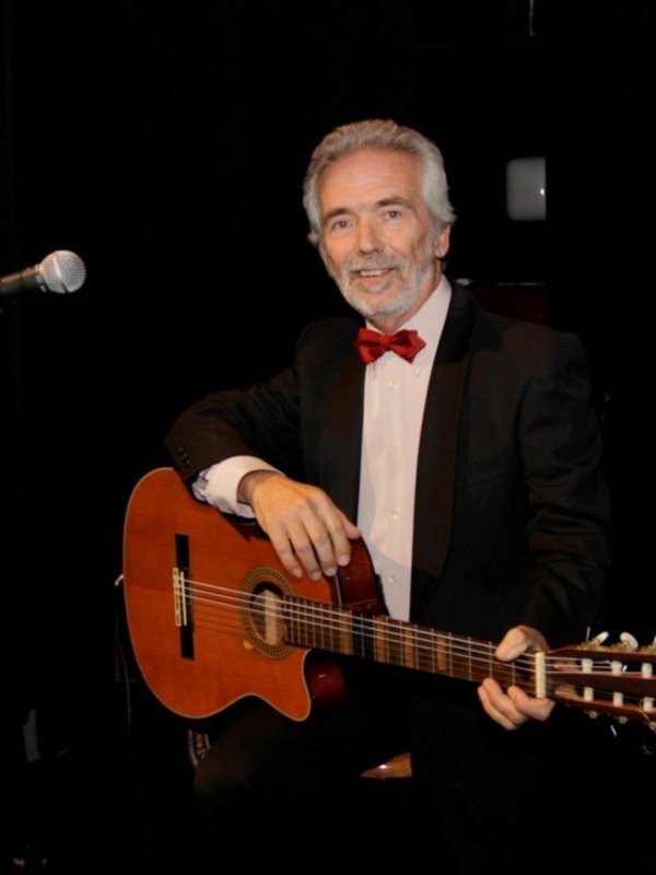 Músico en traje con guitarra clásica, actuando en escenario.