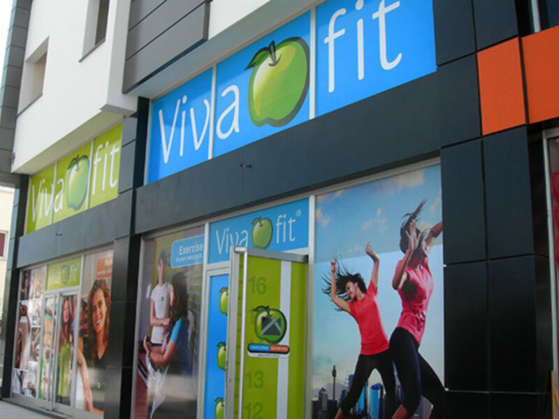 Tienda 'Viva Fit' con anuncios de ejercicio y personas en movimiento en su fachada.