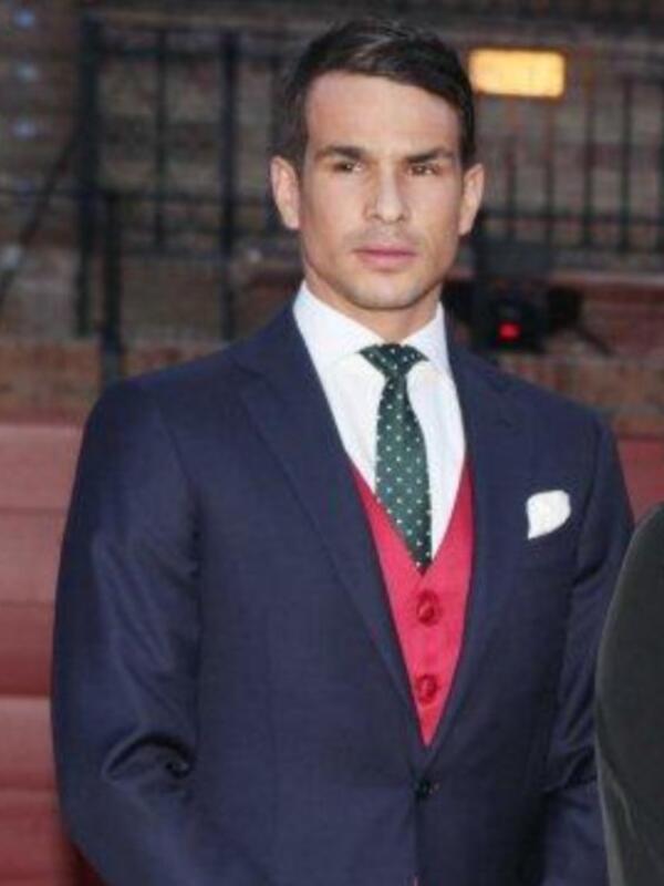 Elegante hombre en traje azul con corbata de lunares verdes y chaleco rojo, posando en una alfombra roja.