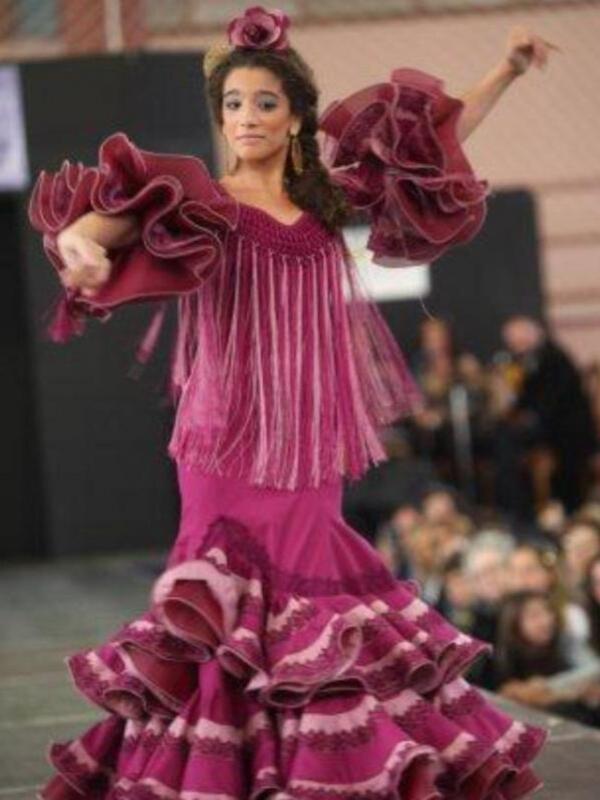 Una bailarina en un vestido de flamenca púrpura con volantes y flecos, bailando en un desfile de moda.