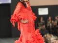 Una mujer vestida con un traje de flamenca rojo, posando en una pasarela.