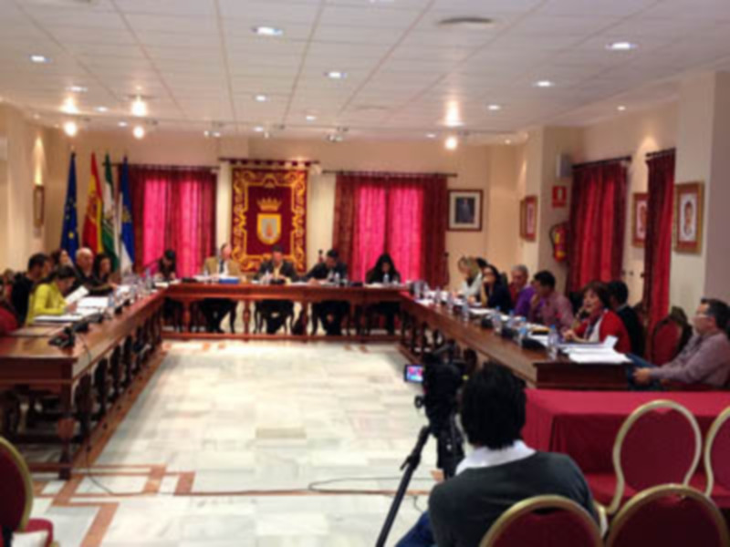 Sala de reuniones con mesas redondas, sillas rojas, cortinas rojas, banderas, y una cámara en el extremo del escritorio.