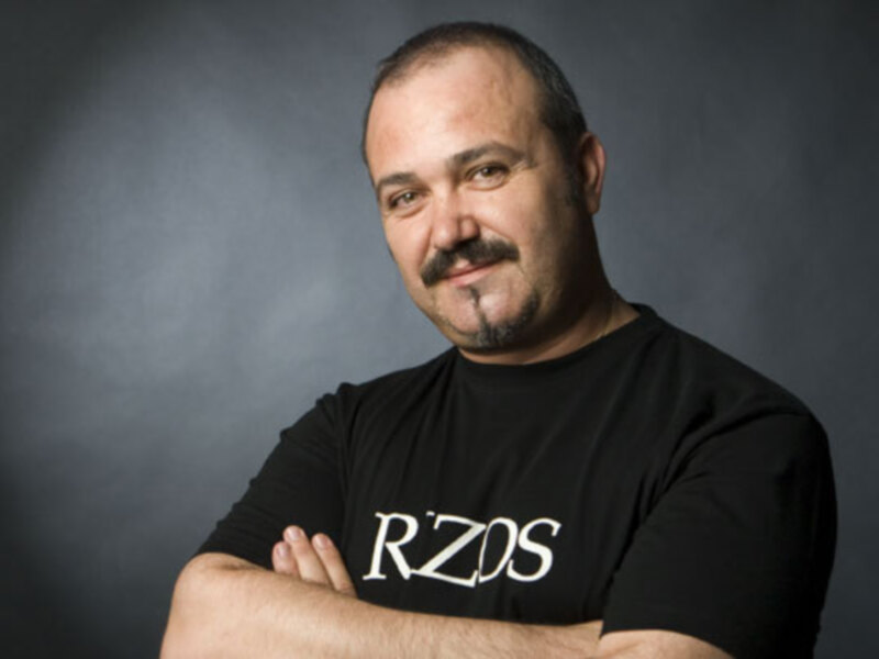 Hombre con camiseta negra y brazos cruzados, fondo oscuro