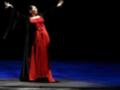 Una bailarina de flamenco en una escena dramática, con un vestido rojo y negro que destaca en el escenario oscuro. La postura y el movimiento sugieren una actuación intensa y emocional.