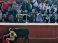 Un torero en chaqueta amarilla y pantalones rojos se enfrenta a un toro negro en una plaza de toros. La audiencia, compuesta por personas vestidas con diferentes estilos, observa la escena desde los asientos. La imagen captura el espíritu de la tradición taurina y la intensidad del enfrentamiento entre torero y animal.