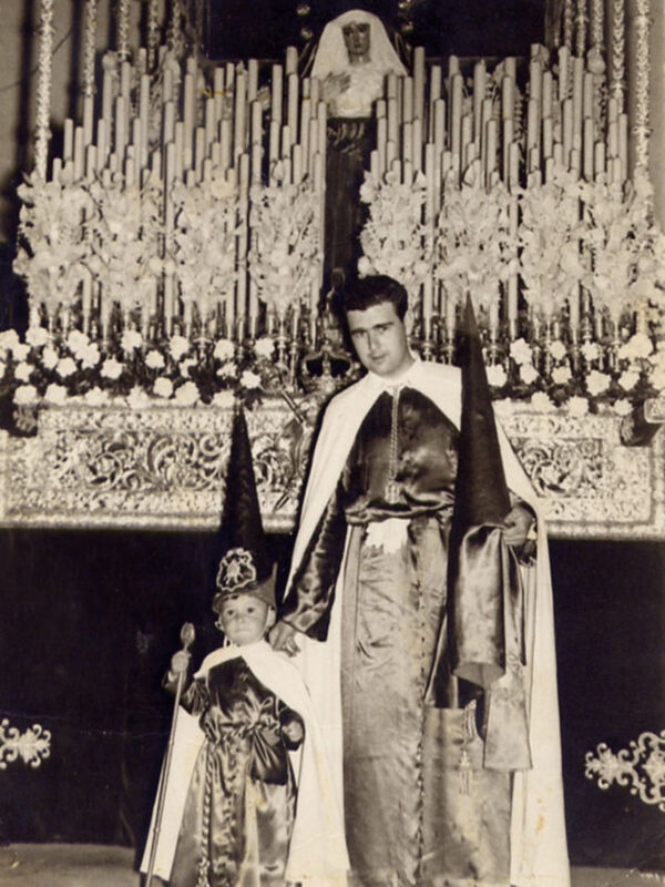 Una familia posa frente a un altar ricamente decorado con flores y velas. La imagen parece ser de una época pasada, posiblemente del siglo XX.
