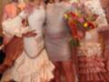 Las mujeres están vestidas con trajes de flamenca coloridos y volantes, posando en un evento formal. La imagen muestra detalles de su vestimenta y expresiones faciales, destacando la belleza y elegancia del traje tradicional español.