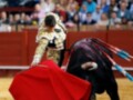 Un torero con capa roja y muleta frente a un toro en una plaza de toros.