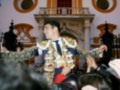 Un torero en traje tradicional celebra con un gesto de victoria, rodeado por una multitud en un entorno festivo.