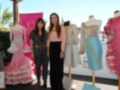 Dos mujeres posan junto a maniquíes con vestidos de colores pastel en un evento de moda.
