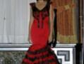 Una modelo presenta un vestido rojo y negro con detalles en negro, diseñado para una fiesta o evento formal.