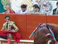 Un torero en traje tradicional sostiene una capa roja mientras un toro se prepara para la matanza en una plaza de toros.