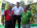 Tres hombres posan con medallas en un podio, uno de ellos con una bandera amarilla y verde detrás.