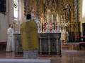 Un sacerdote bendice en una iglesia con un altar adornado con velas y estatuas religiosas.