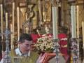 Un sacerdote en actitud de oración durante una ceremonia religiosa en un altar ricamente decorado.