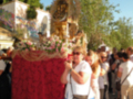 Una procesión religiosa con una imagen de la Virgen en un carro decorado, acompañada por varias personas.
