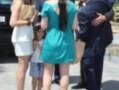 Una joven en un vestido verde está caminando con otros dos adultos y una niña. La escena parece ser en un evento formal o ceremonial, con personas vestidas de manera elegante y una cartera visible.