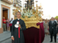 Procesión religiosa con sacerdote y estandarte en una calle de pueblo.