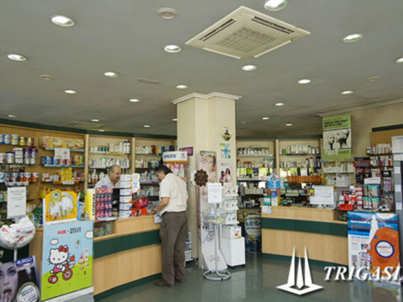 Interior de una farmacia con estantes bien organizados y clientes intercambiando información con el personal de atención al cliente.