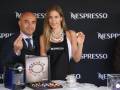 Un hombre y una mujer posan con un café en una conferencia de prensa. El fondo es negro con el logotipo de Nespresso.