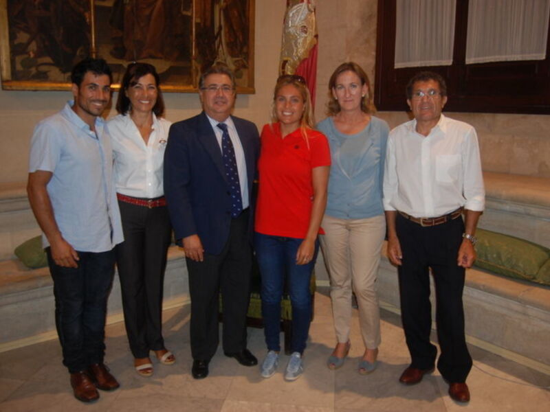 Grupo de personas posando para una foto en un entorno formal con un fondo de pintura histórica y bandera.