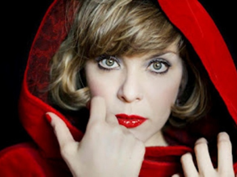 Mujer con capucha roja y labios rojos, gesto pensativo sobre el rostro.