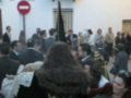 Procesión de Semana Santa en una calle de España, con participantes en trajes tradicionales y una figura procesional en el centro.