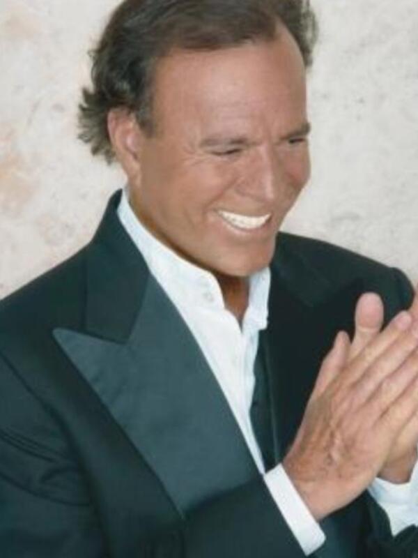 El cantante español Julio Iglesias sonríe ampliamente mientras aplaude con entusiasmo. Su expresión de alegría y emoción es evidente en cada gesto, reflejando su pasión por la música y el entusiasmo que transmite a sus seguidores.