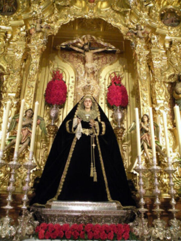 Retablo dorado con imagen de la Virgen de la Soledad y candelabros de plata, típico de la Semana Santa en España.