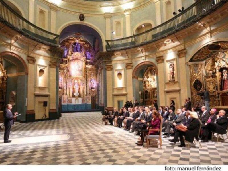 Interior de una iglesia barroca con una audiencia en el piso inferior y un altar majestuoso en el fondo.