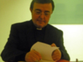 Persona en traje sacerdotal escribiendo en un cuaderno sobre una mesa roja.