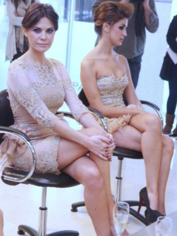 Dos mujeres sentadas en sillas de oficina, vestidas con elegantes vestidos de fiesta, posando en un evento social.