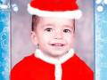 Un niño sonríe mientras lleva un sombrero rojo y una chaqueta de Santa Claus. El fondo es azul con copos de nieve y dos pequeños ángeles en la parte superior.