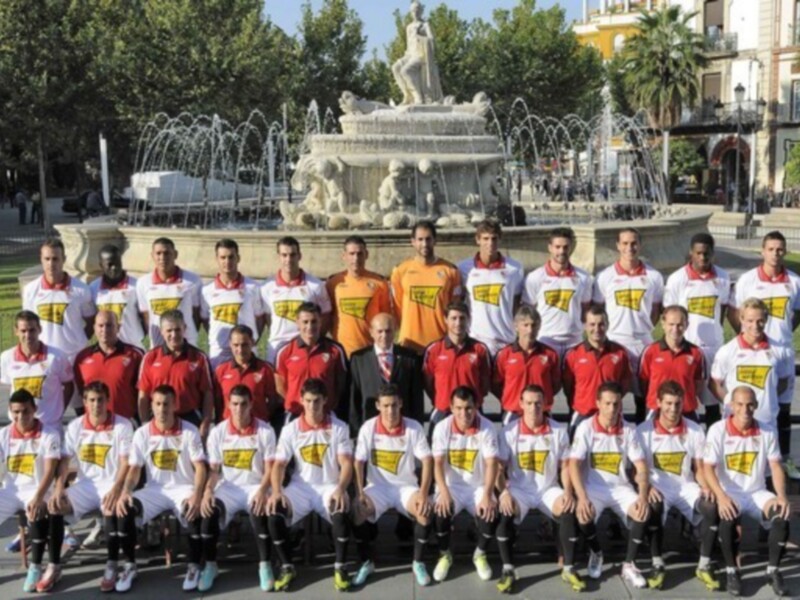Equipo de fútbol posando en frente de una fuente ornamental en un parque.