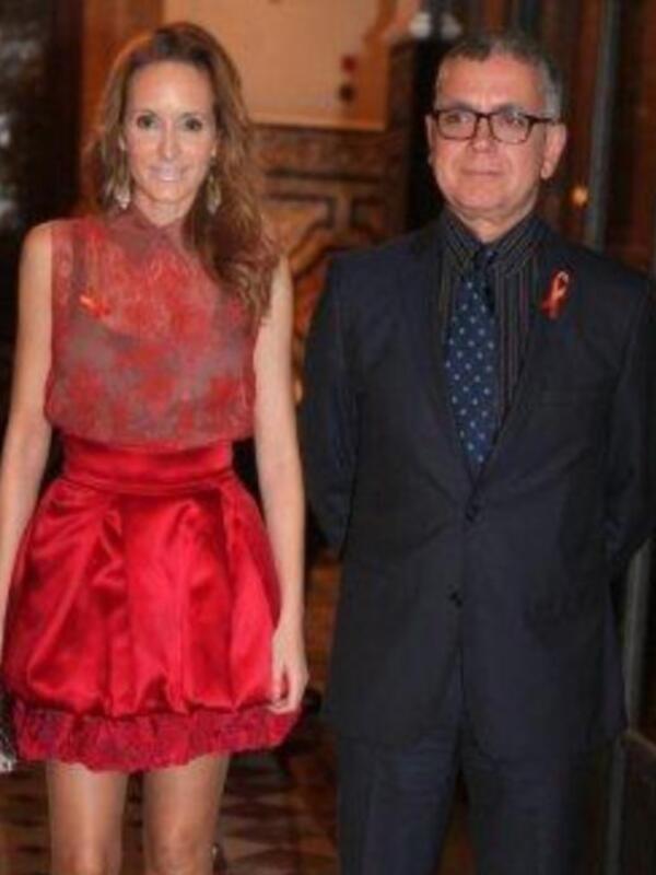 Una pareja elegante posa juntos en un evento formal, ella con un vestido rojo y él en traje negro con corbata de lunares.