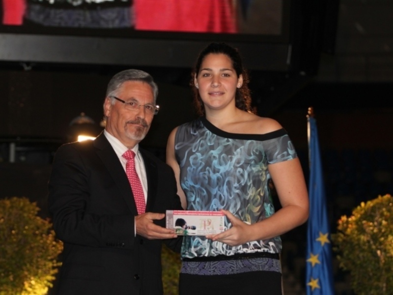 Entrega de premio en un evento formal con bandera de la Unión Europea en el fondo.