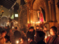 Interior de una iglesia con personas rezando, velas encendidas y una imagen religiosa en el altar.