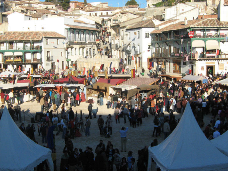 Mercado tradicional en una plaza histórica con puestos de venta y multitud de visitantes.