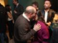 Amor y cariño entre un hombre y una mujer en una fiesta, con otros asistentes en el fondo.